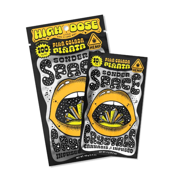 Two packets of Sonder Space THC Crystals in Piña Colada Piñata flavor, labeled with 100 mg and 10 mg THC respectively, featuring bold graphic design with a mouth and crystals illustration.